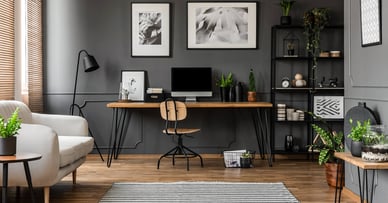 A photo of a home office with dark walls and the computer and desk in the center on the wall. 