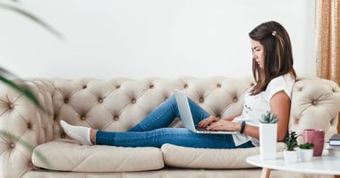 A woman lounges on her couch, working from home on her laptop. 