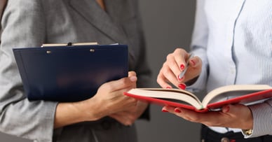 A woman holding a clipboard, and then another woman with a red book.