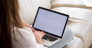 A woman sits on a couch and types on laptop computer.