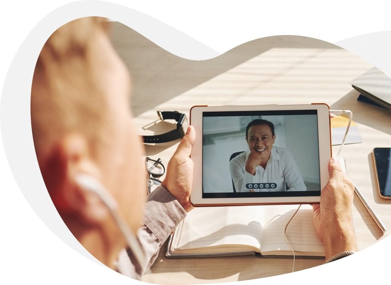 Image of man holding a tablet as he talks to that person on the device. 