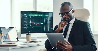 Technology's Impact on Driving Investment Success - Business Man Looking at Tablet at Computer Desk