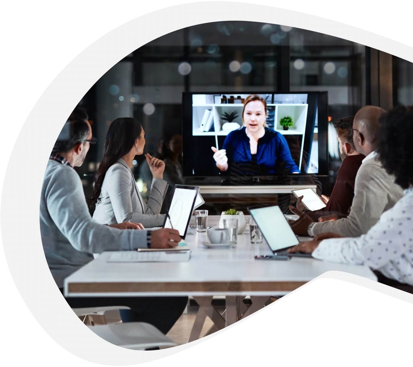 A group of employees talk with a woman on a video chat. 